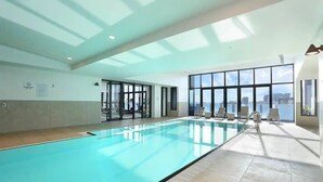 A large indoor swimming pool with clear blue water, surrounded by sunlit rooms and large windows offering views of the city. - A Cozy & Modern 2BR Apartment, Fantastic Views (Melbourne)