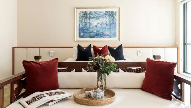 A cozy room with a bed, a bedside table with a vase of flowers, and a painting on the wall. - Stylish & Cozy 4BR Retreat With Free Parking (Melbourne)