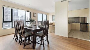 A spacious dining area with a wooden table and chairs, large windows, and a modern kitchen with stainless steel appliances. - Stylish & Cozy 4BR Retreat With Free Parking (Melbourne)