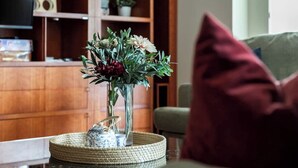 A living room with a wooden cabinet, a television, and a vase with flowers on a table. - Stylish & Cozy 4BR Retreat With Free Parking (Melbourne)