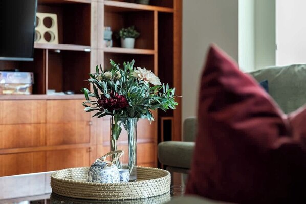 Ein Wohnzimmer mit einem Holzkasten, einem Fernseher und einer Vase mit Blumen auf einem Tisch.