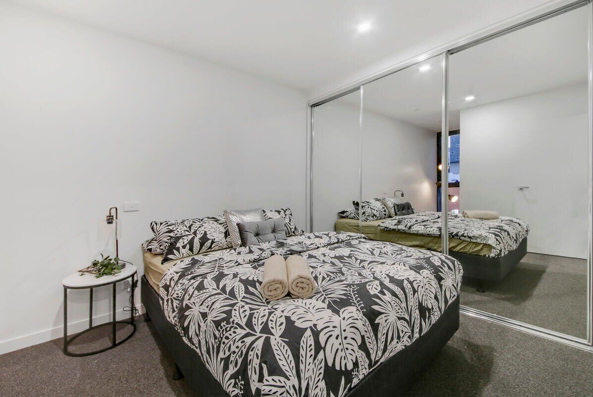 Ein modernes Schlafzimmer mit einem großen Bett, einem kleinen Nachttisch und einem großen Spiegel.