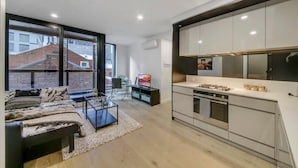 Eine moderne Wohnung mit Küche, einem Wohnbereich mit Sofa und Couchtisch sowie großen Fenstern mit Blick auf die Stadt.