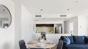 A modern living room with a dining area, a sofa, and a kitchen in the background.