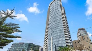 A modern high-rise building with a curved facade, surrounded by other buildings and palm trees.