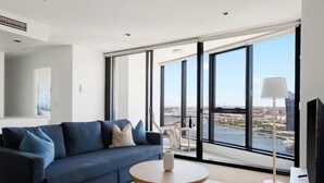 A modern living room with a blue sofa, a round wooden coffee table, and a large window offering a city view.