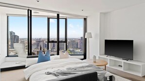 A modern hotel room with a large bed, a TV, and a city view.
