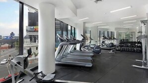 A gym with treadmills, weight machines, and a large window offering a city view.