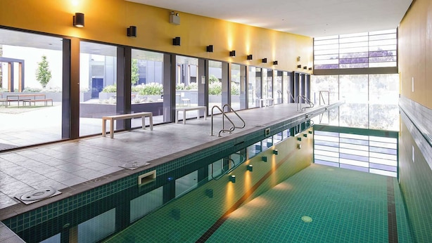 A modern indoor swimming pool with clear glass walls, benches, and metal handrails. - A 2BR Apt in Parkville Near the Melbourne Zoo (Melbourne)