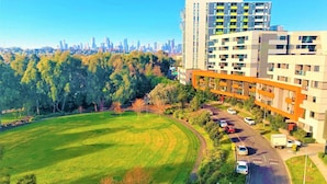 A modern apartment complex with a green park and a city skyline in the background. - A 2BR Apt in Parkville Near the Melbourne Zoo (Melbourne)