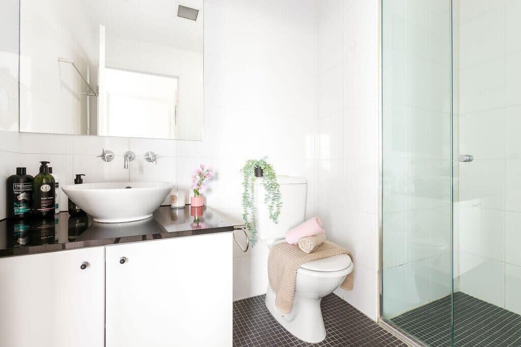 Un baño con lavabo blanco, espejo, inodoro y cabina de ducha con mampara de vidrio.