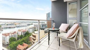 Un balcon donnant sur un paysage urbain, une table avec un vase et une chaise avec une couverture.