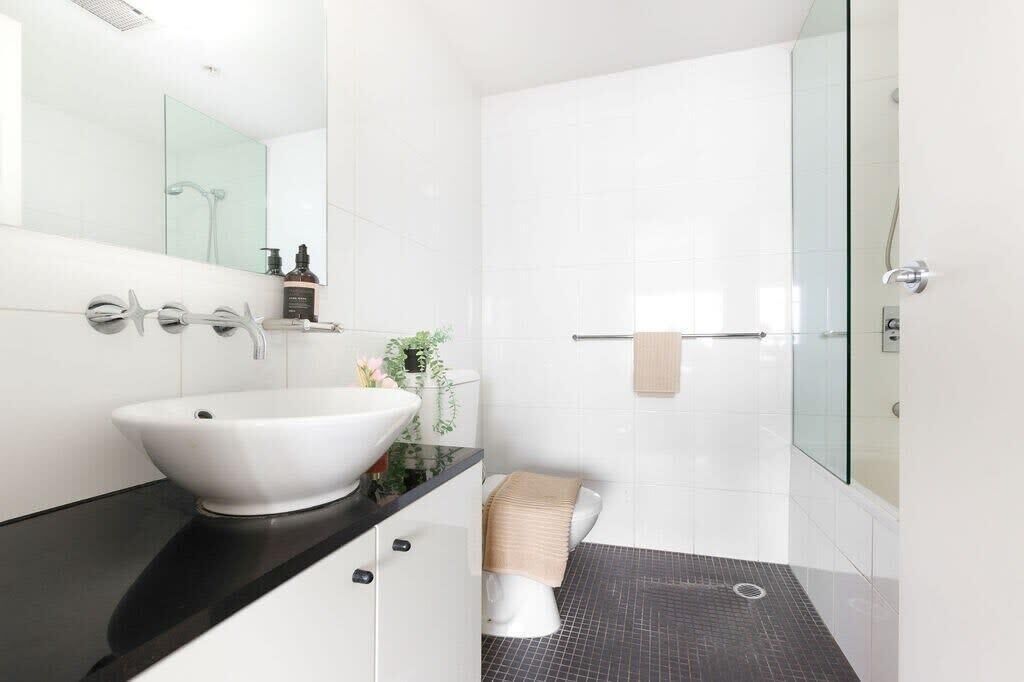 A modern bathroom with a large white sink, a glass shower enclosure, and a black tiled floor.