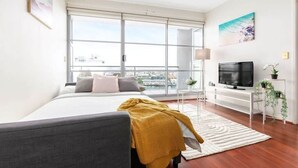 Une chambre moderne avec un grand lit, une télévision et un balcon offrant une vue sur la ville.
