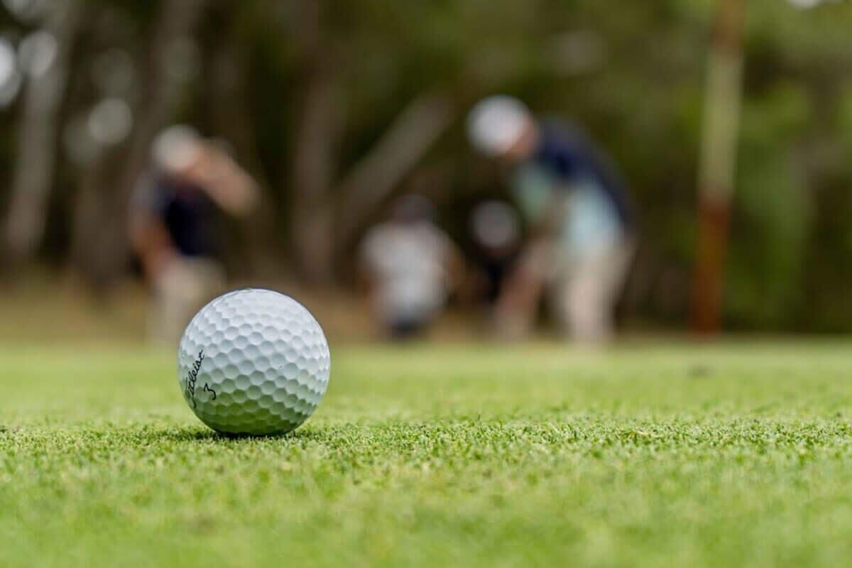 Ein Golfball auf einer Grünfläche, im Hintergrund verschwommene Personen.