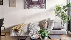 Un salon moderne avec un canapé, une table basse sur laquelle repose un livre, et un grand tableau encadré représentant la Tour Eiffel.