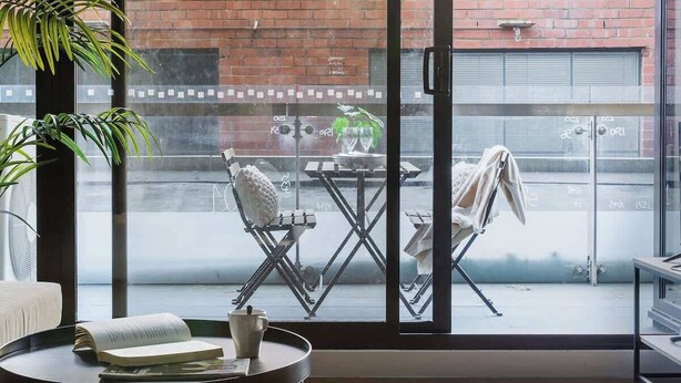 Une chambre moderne avec de grandes fenêtres, une table ronde sur laquelle se trouvent un livre et une tasse, et une plante en pot.