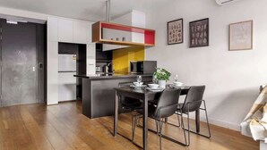 Une cuisine moderne avec des meubles blancs, un mur d’accent jaune et un coin repas avec une table dressée pour deux personnes.