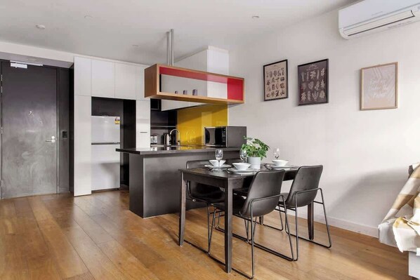 A modern kitchen with white cabinets, a yellow accent wall, and a dining area with a table set for two.