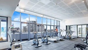 A modern gym with various cardio machines, large windows offering city views, and a spacious layout. - City View 2br, Free Parking, Bright & Central Apt (Melbourne)