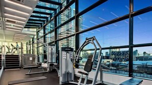 Une salle de sport équipée de matériel d’exercice, dotée de grandes fenêtres et offrant une vue sur la ville.