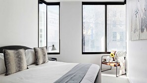 Un dormitorio moderno con una cama grande, dos ventanas, una silla y una lámpara.