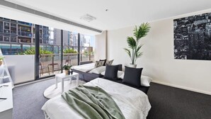 Una habitación de hotel moderna con una cama grande, un balcón con vista a la ciudad y una planta en maceta.