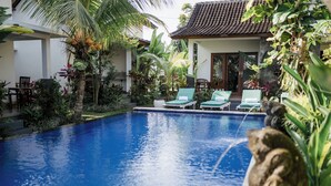 A swimming pool with lounge chairs, surrounded by lush tropical plants and a traditional building. - Sundhara View Ubud (Sukawati)