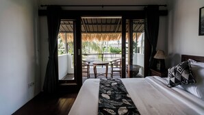 A bedroom with a bed, a nightstand, a lamp, and a view of an outdoor area with a table and chairs. - Sundhara View Ubud (Sukawati)