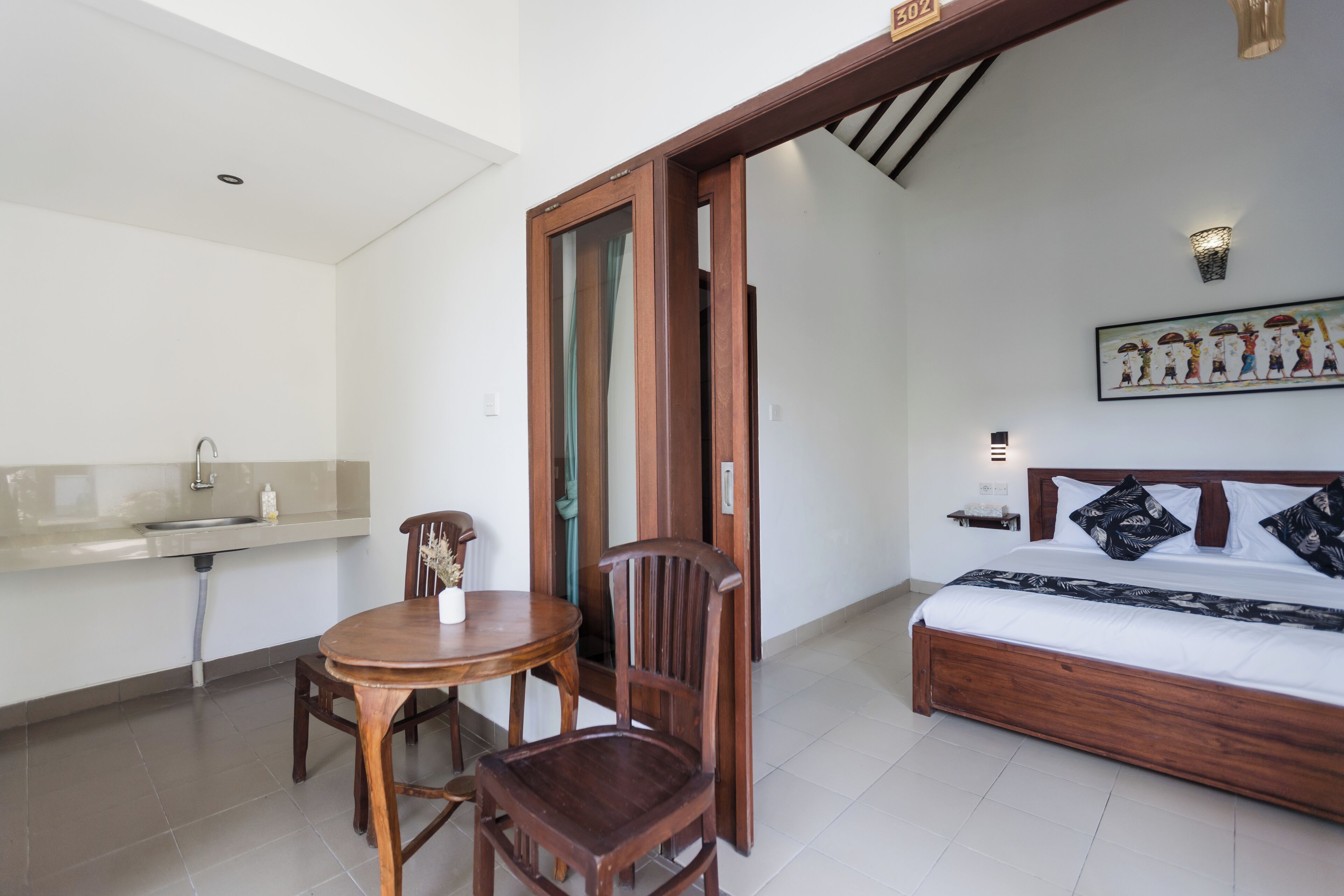 A bedroom with a bed, a wooden chair, a small table, and a bathroom with a sink.