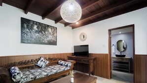 A living room with a wooden sofa, a coffee table, a television, and a decorative wall hanging. - Sundhara View Ubud (Sukawati)