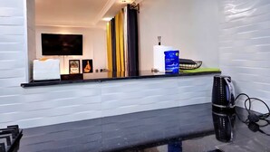 Een moderne keuken met een zwart aanrecht, een flatscreen televisie erboven en diverse keukenbenodigdheden, waaronder een fles afwasmiddel en een waterkoker.