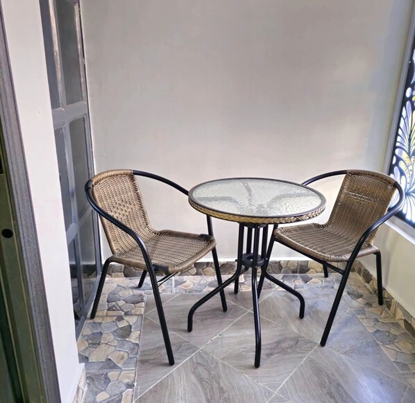 A small outdoor seating area with a round glass table and two wicker chairs.