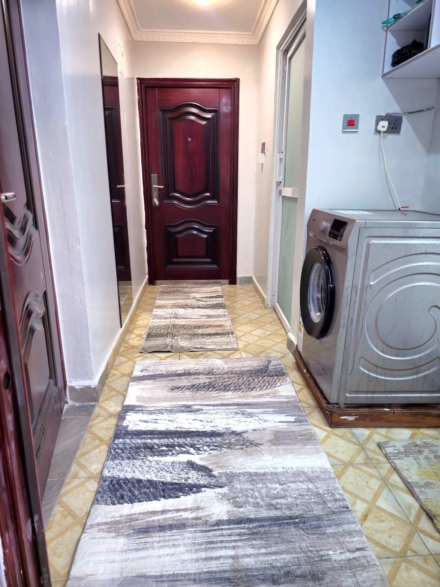 A hallway with a patterned rug, a washing machine, and a door.