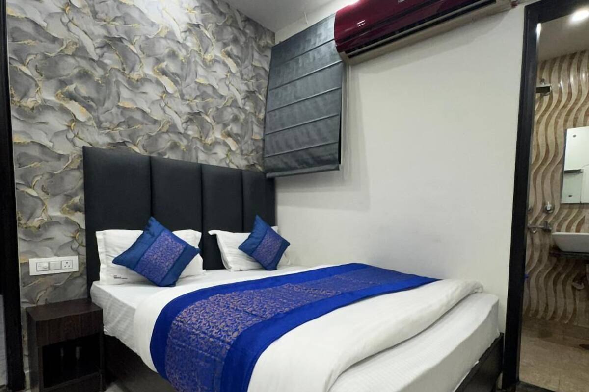 Un dormitorio moderno con pared de diseño de mármol, cabecero negro y colcha azul.
