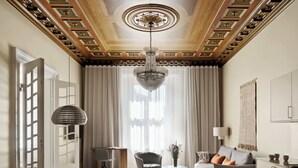 A spacious living room with a chandelier, a sofa, a dining table with chairs, and a large window with curtains.