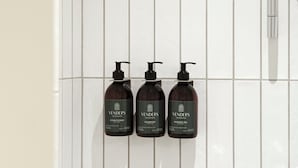 Three Venders Copenhagen products: conditioner, shampoo, and shower gel, mounted on a tiled wall.