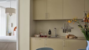 A modern kitchen with a dining area, featuring a wooden table with a plate of food, a sink with utensils, and a vase of flowers.