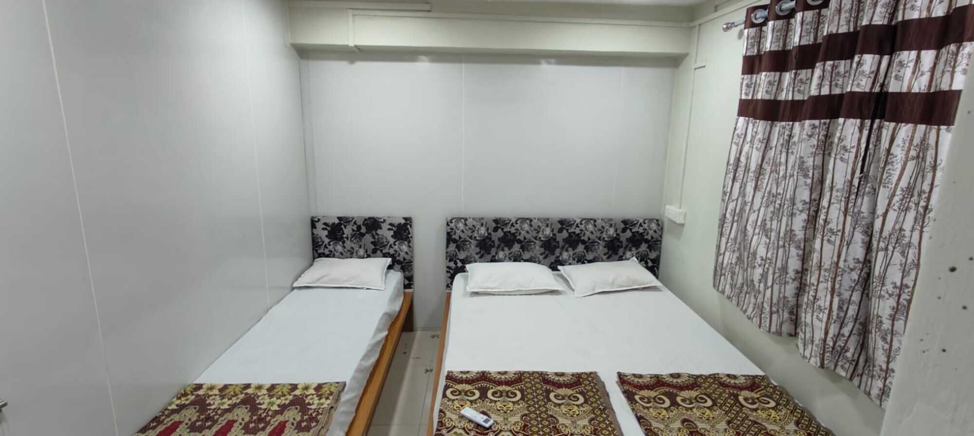 A small, clean room with two single beds, white bedding, and patterned curtains.
