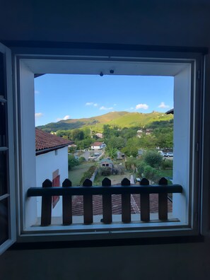 A view from a window with a balcony, overlooking a residential area with houses, greenery, and a hill in the distance. - Apartment 'Tamburine Xaharra' with Mountain View and Wi-Fi (Ainhoa)
