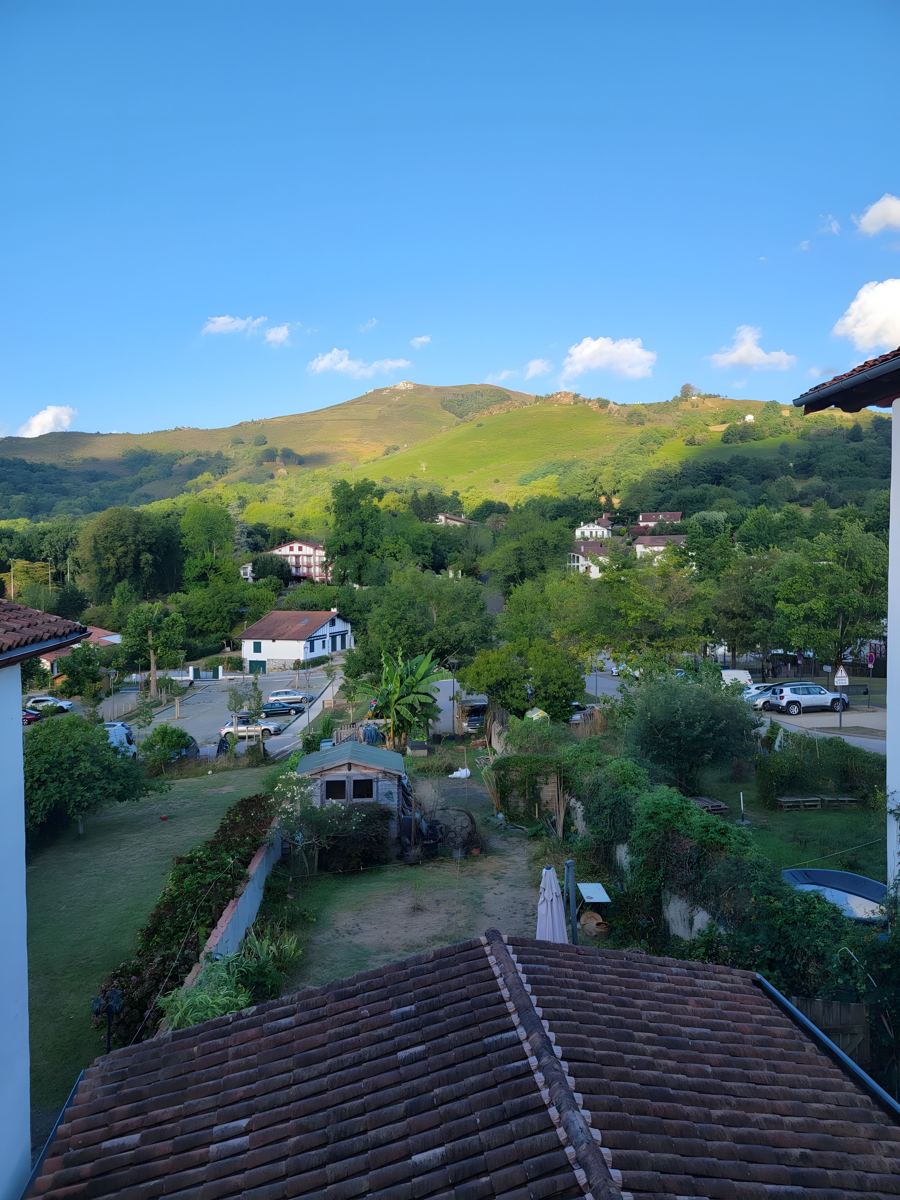 A residential area with houses, a street, and a hilly landscape in the background.