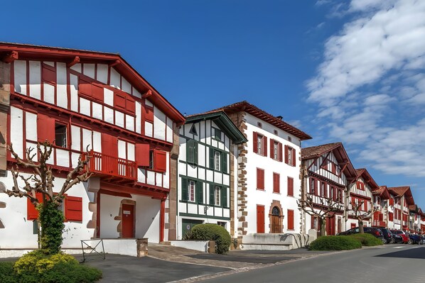 A row of traditional half-timbered houses with red and white facades, a clear sky, and a paved street.