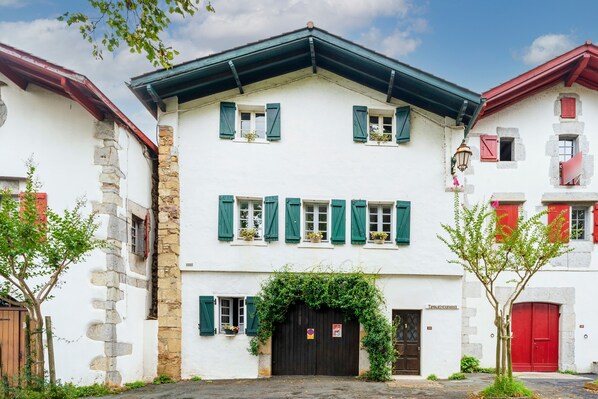 A two-story building with a white facade, green shutters, and a black entrance door.