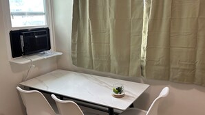 Un comedor con una mesa blanca y cuatro sillas blancas, un estante con un radiador y un ventanal con vistas al exterior.