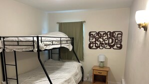 Dormitorio con literas, mesita de noche de madera y un adorno en la pared.