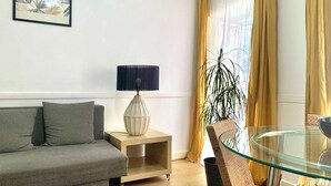 A modern living room with a grey sofa, a side table with a lamp, a glass table, and a potted plant. - Central Avenue #1 (Lisboa)