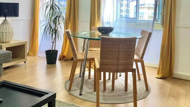 A modern living room with a glass dining table, wicker chairs, a potted plant, and a black coffee table. - Central Avenue #1 (Lisboa)