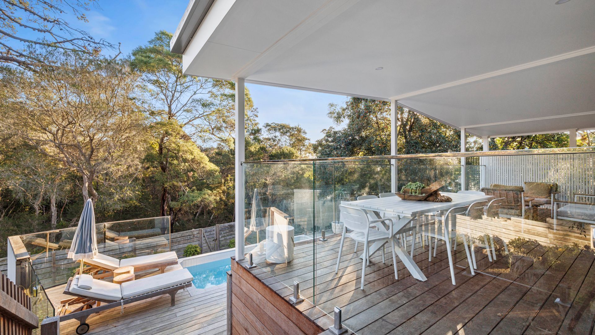 Eine moderne Außenterrasse mit Glasveranda, Holzmöbeln und einem Pool.