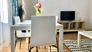 A modern living room with a white table, a TV on a wooden stand, and a vase with flowers. - Central Avenue #2 (Lisboa)