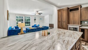 A spacious living area with a large marble dining table, a blue sofa set, wooden cabinets, and a ceiling fan. - Welcoming 3-bedroom home with jacuzzi (Winterport)